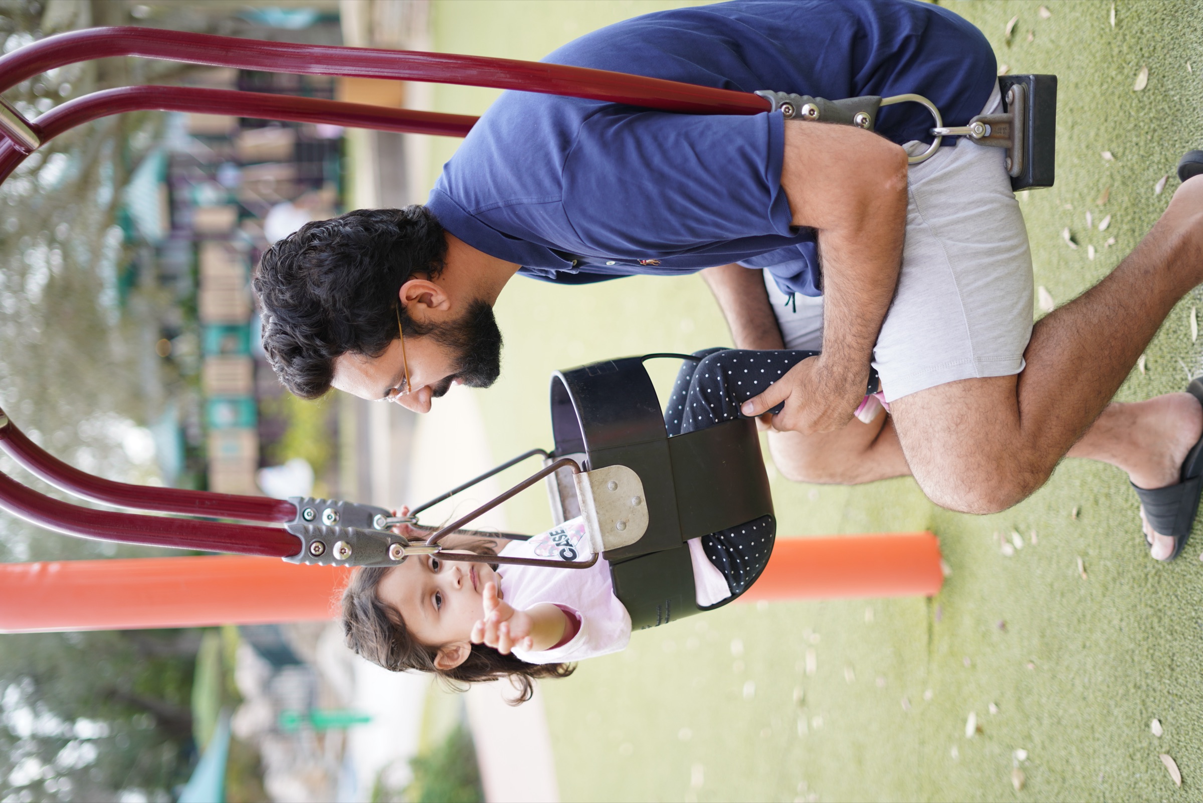 Dad crouching to talk with his daughter in a playground swing