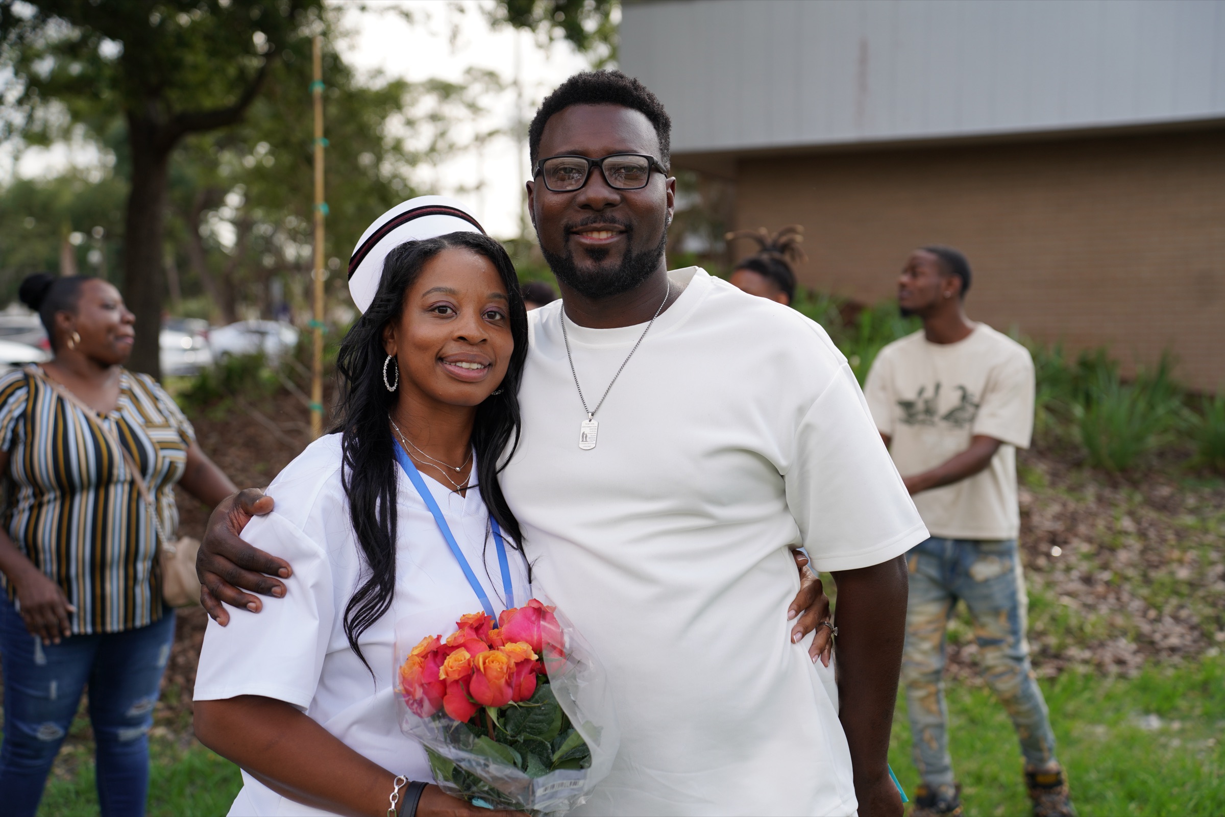 New nurse holding roses, hugged by her husband after her pinning ceremony