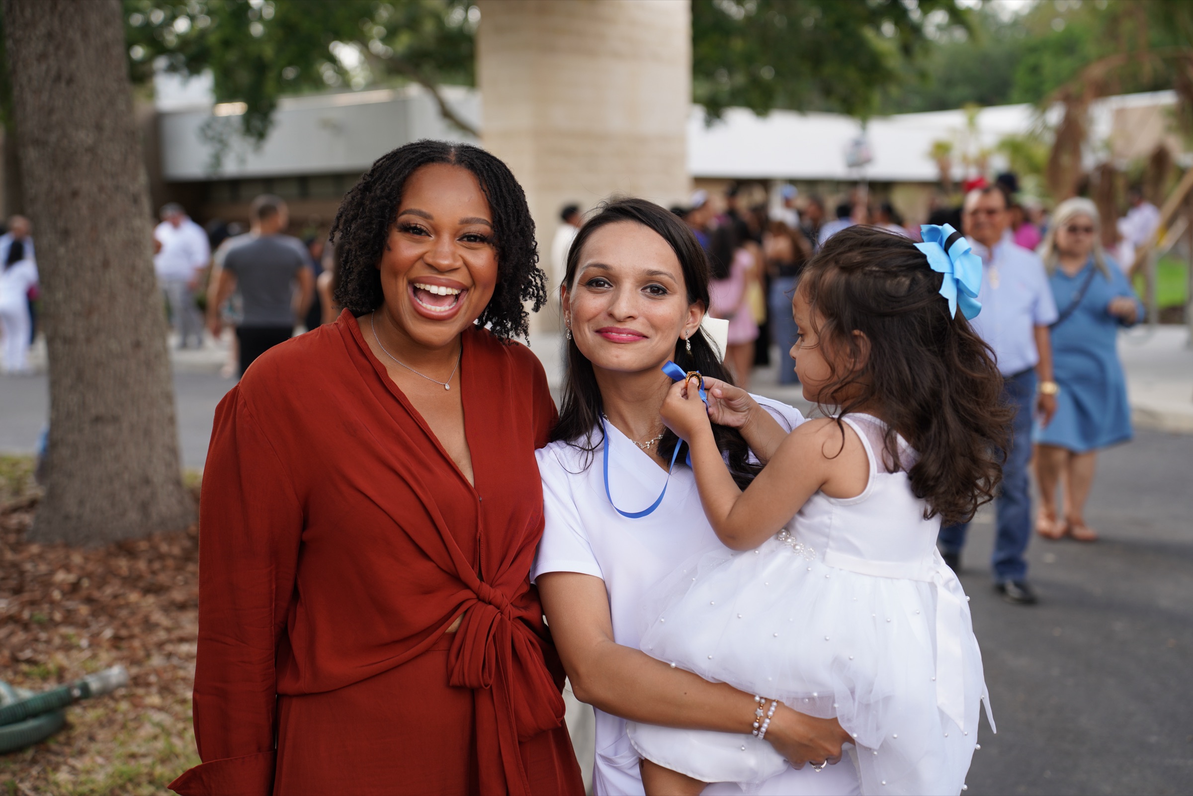 Two friends laughing outside a pinning ceremony, one holding her daughter