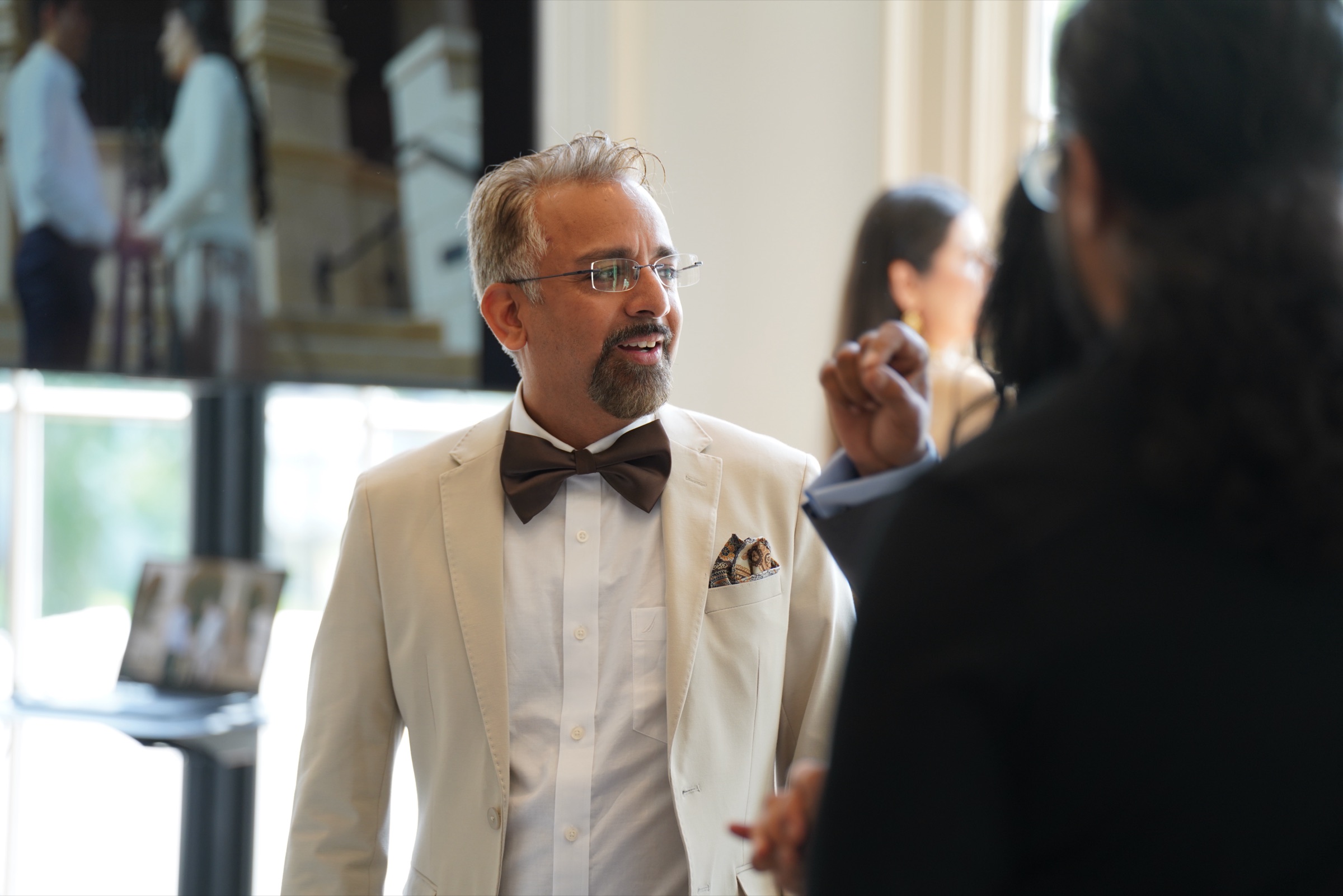 Wedding guest in a cream jacket and brown bow tie mid-conversation