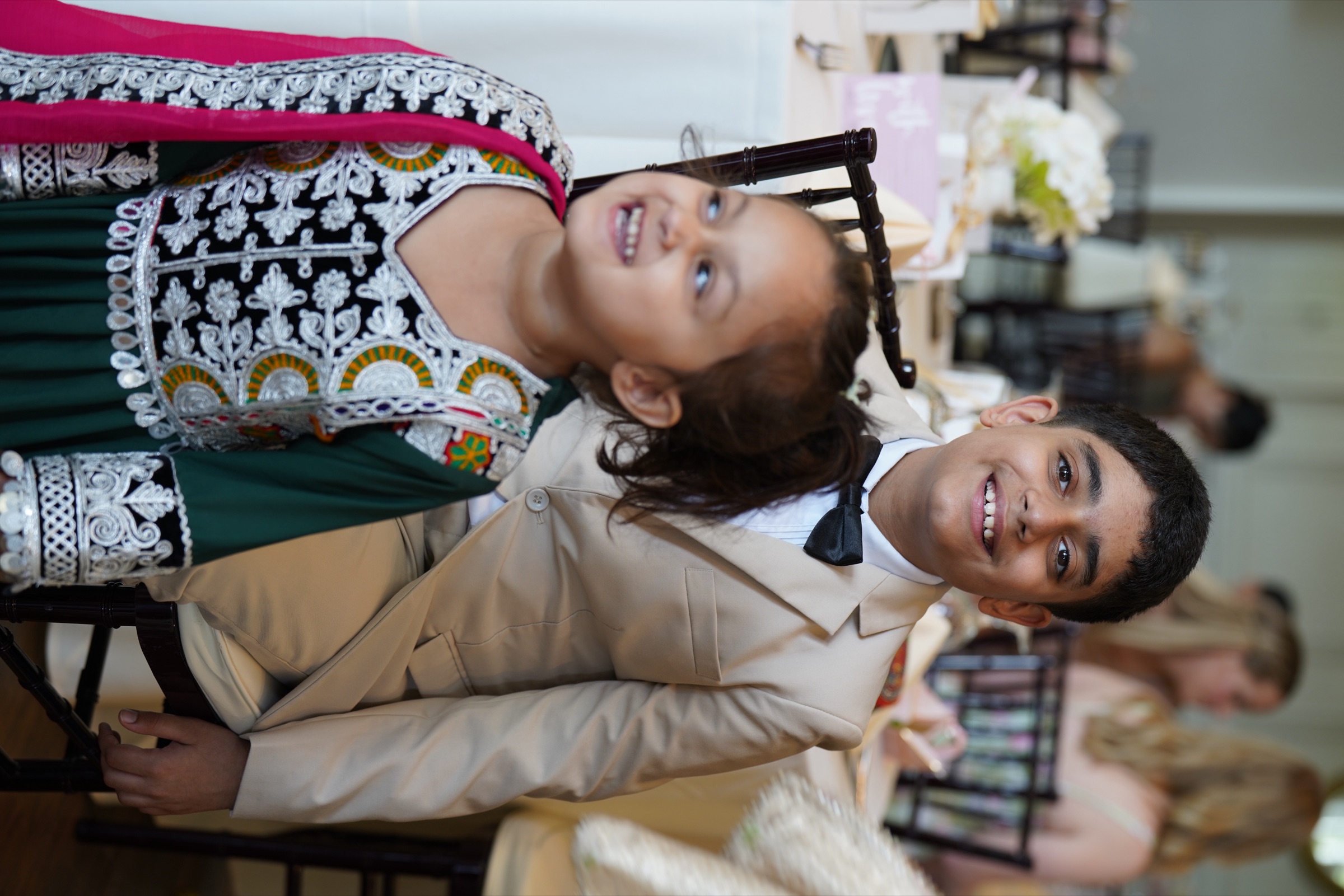 Big brother in a bow tie and little sister in traditional dress cracking up at the reception