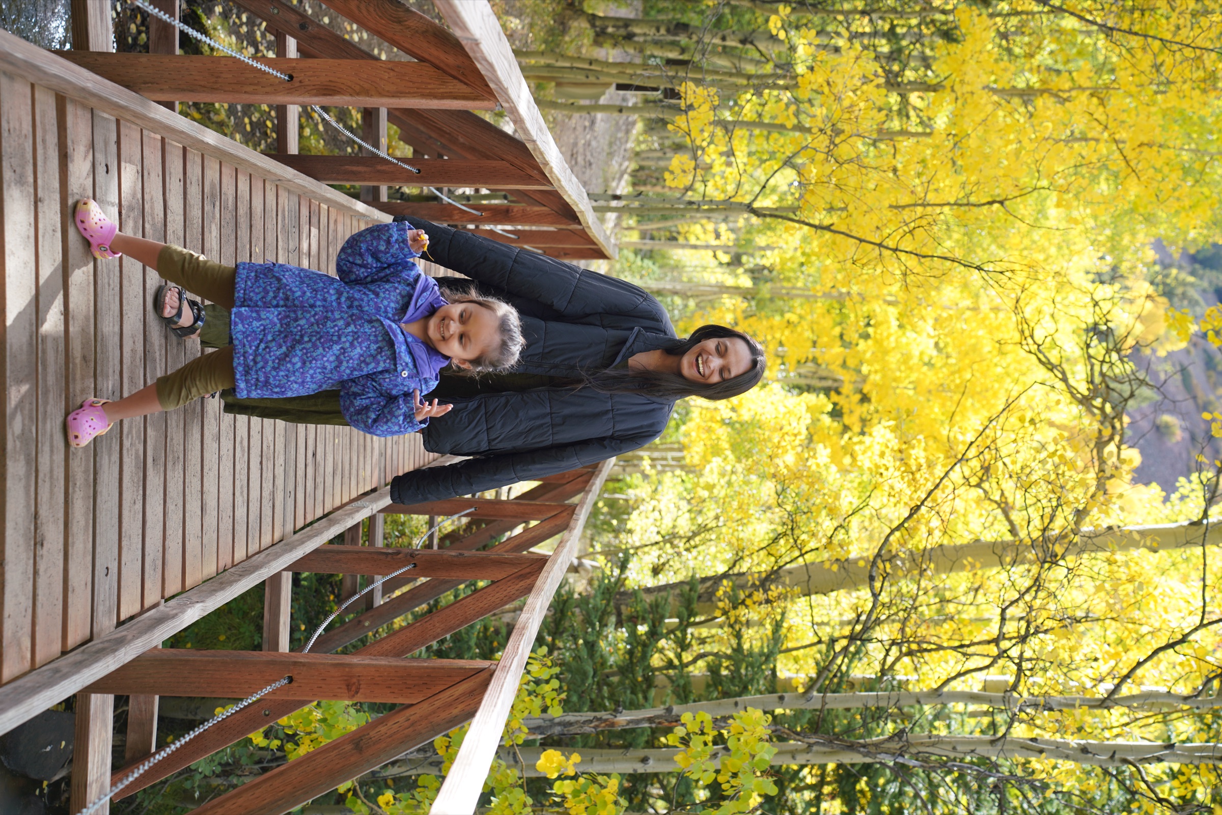 Mom and daughter on a wooden footbridge under blazing yellow aspens