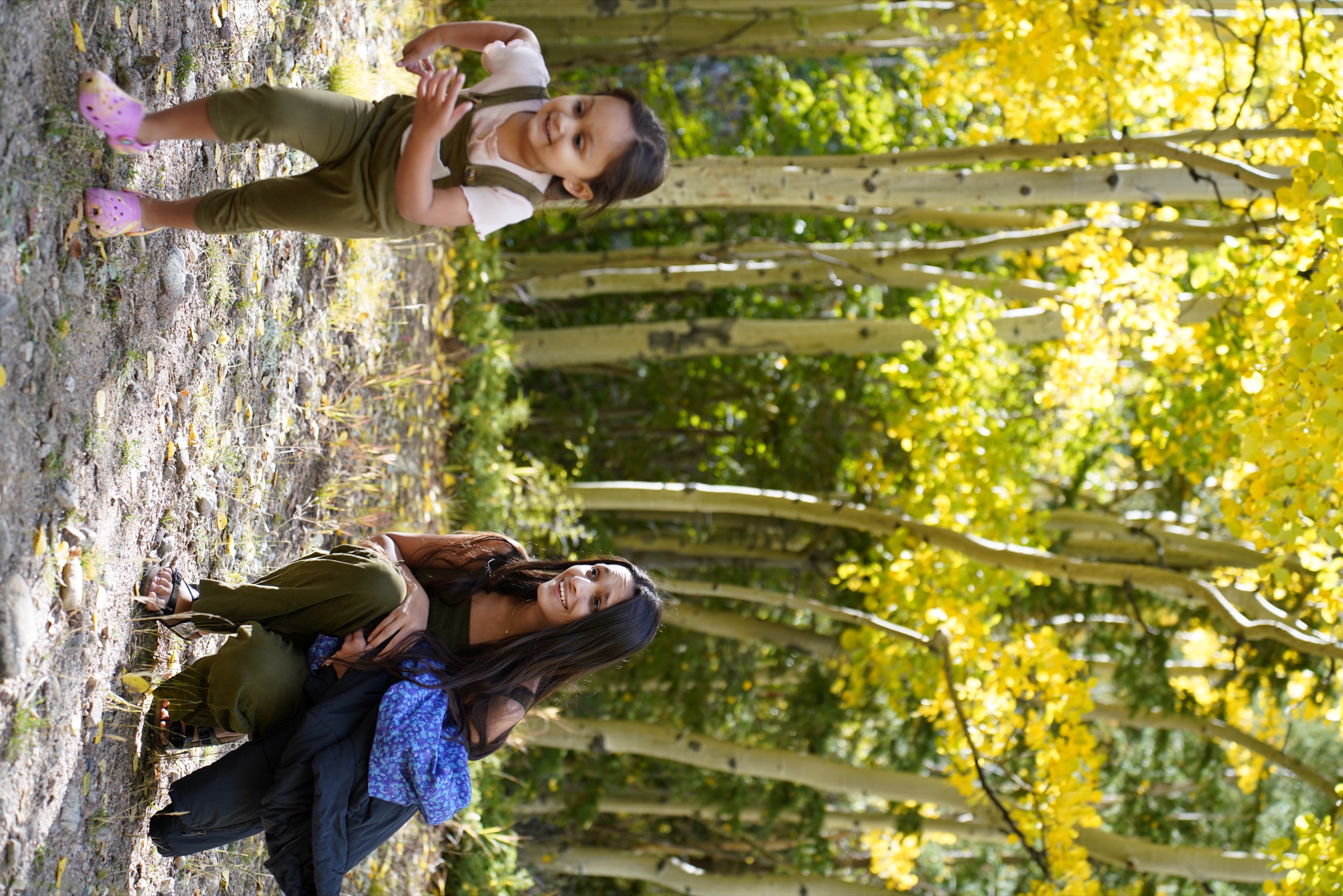 Girl bolting away while mom laughs behind her in an aspen grove