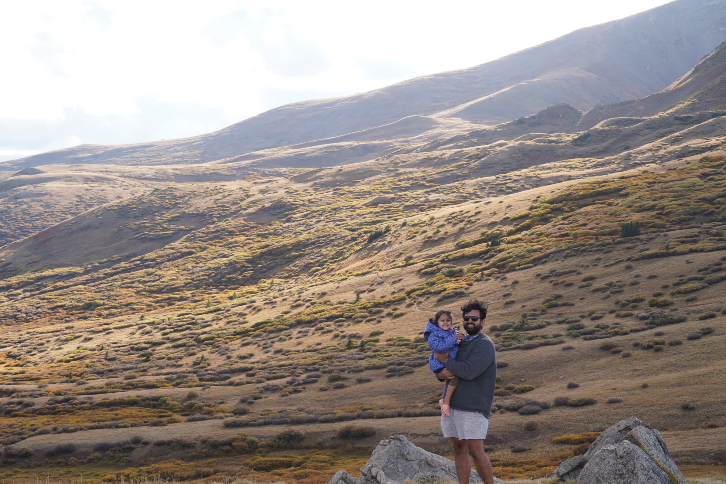 Dad holding daughter on a rock below a vast alpine tundra hillside