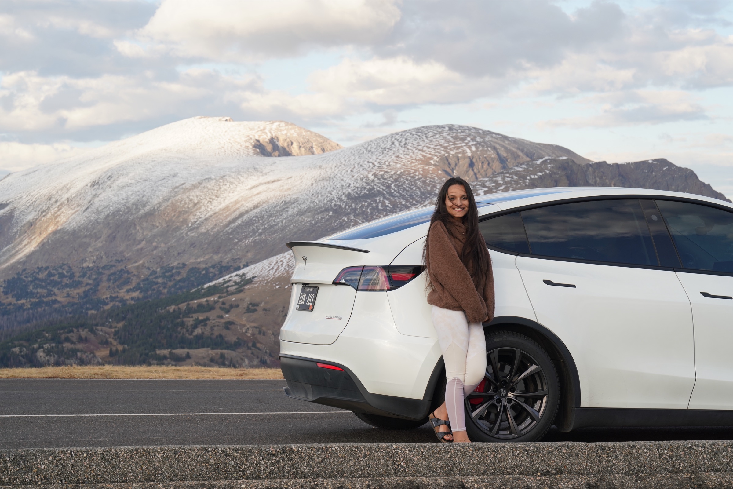 White Tesla and its owner in front of a snow-dusted peak on Trail Ridge Road