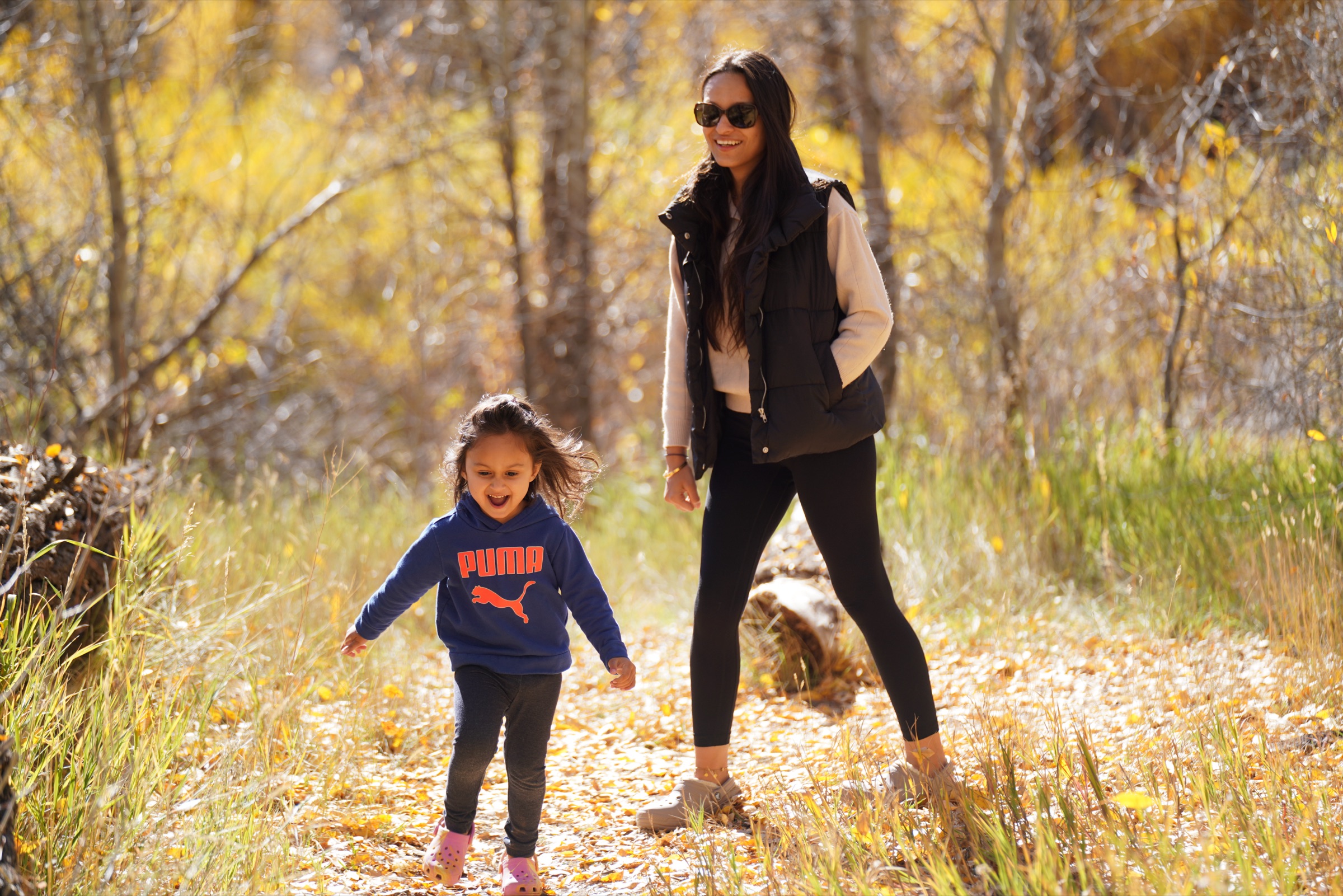 Mom and daughter walking a leaf-covered path in fall