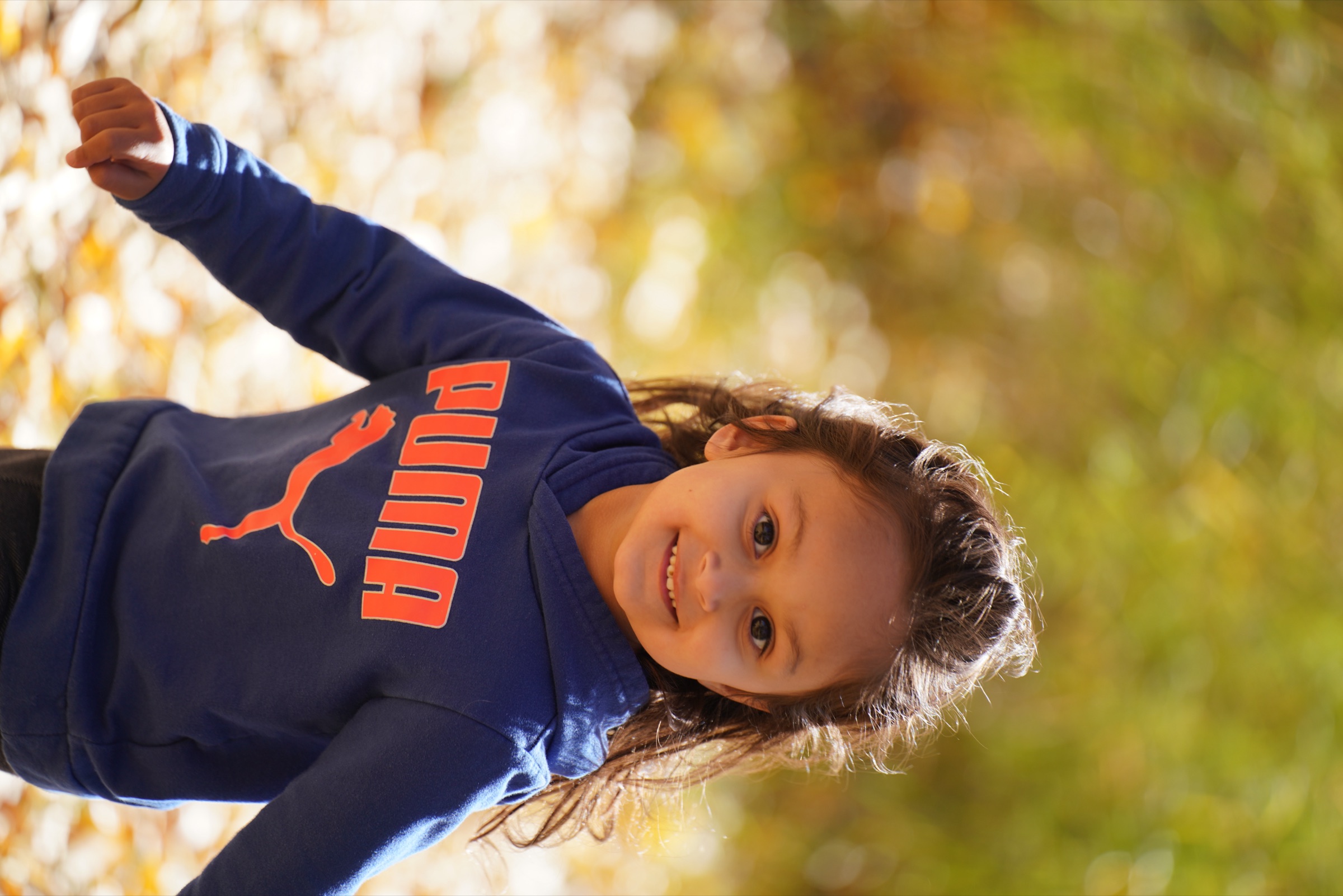 Girl in a blue Puma hoodie running through golden leaves, grinning